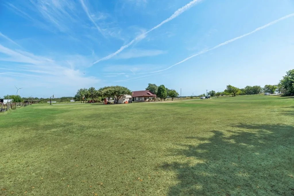 Expansive green lawn with mature trees and a single-story residence featuring a red roof