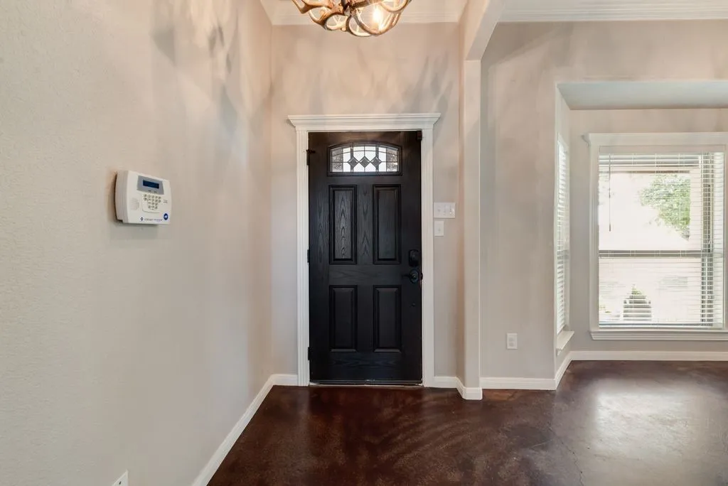 Dark wood entry door with decorative glass, two windows with blinds, and rich, dark flooring