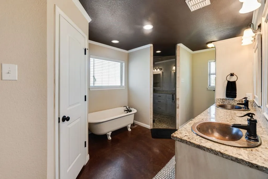 Spa-inspired primary bathroom featuring a freestanding soaking tub with a window, walk-in shower with tile surround, dual vanity with granite countertop and undermount sink, dark wood-finish flooring, and recessed ceiling lighting