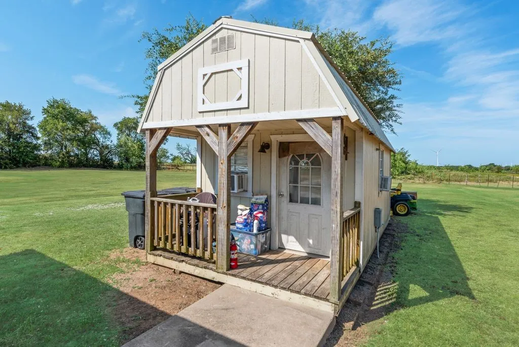 Detached outbuilding featuring a gambrel roof and covered porch with wood railing