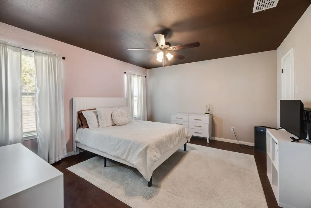 Wood-finish flooring with a contrasting ceiling, dual windows with blinds, and a built-in ceiling fan with lighting