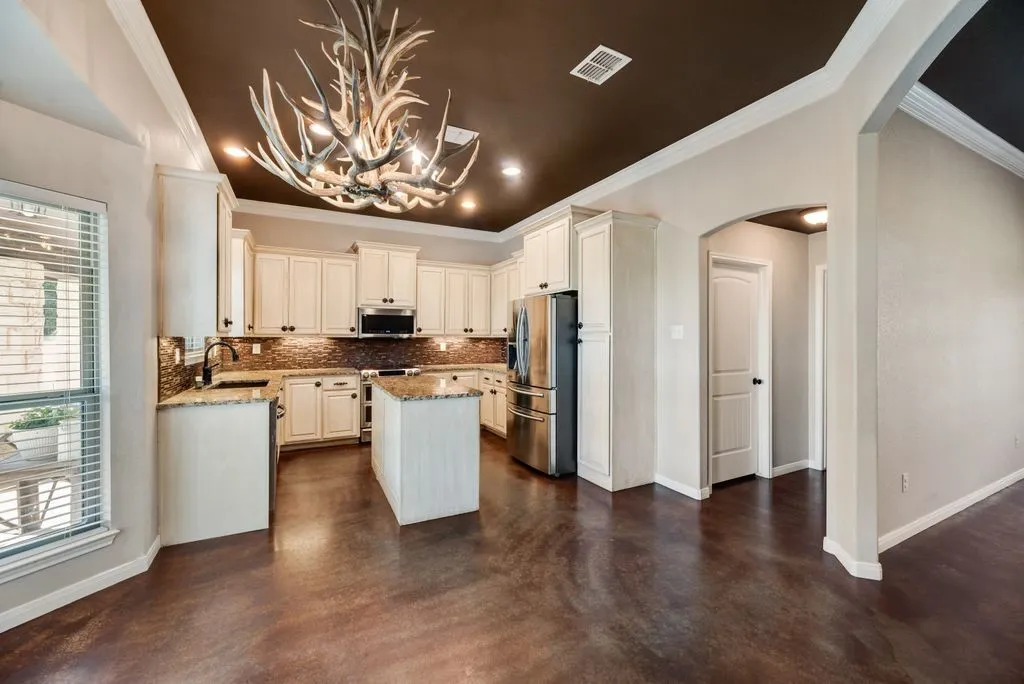 Kitchen featuring an antler chandelier, cream cabinetry, a center island, brown tile backsplash, and stainless steel appliances