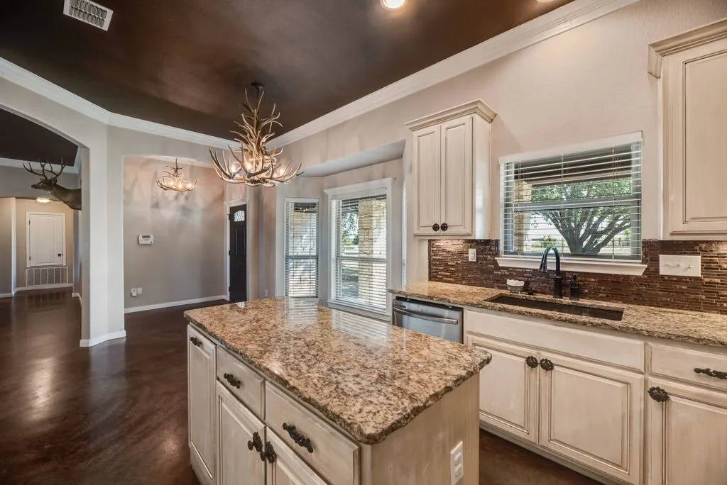 Kitchen featuring an island with granite countertops, light cabinetry, a tile backsplash, and a built-in sink with a gooseneck faucet