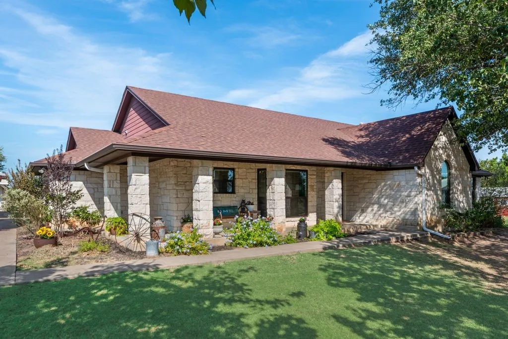 Charming residence featuring a stone and brick exterior with covered front porch supported by classical columns, peaked roofline with multiple gables, and manicured lawn with mature landscaping and shade trees
