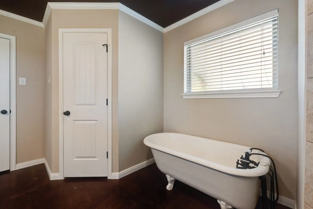 Freestanding clawfoot tub with a dark bronze faucet, wood-finish flooring, white horizontal blinds, and crown molding