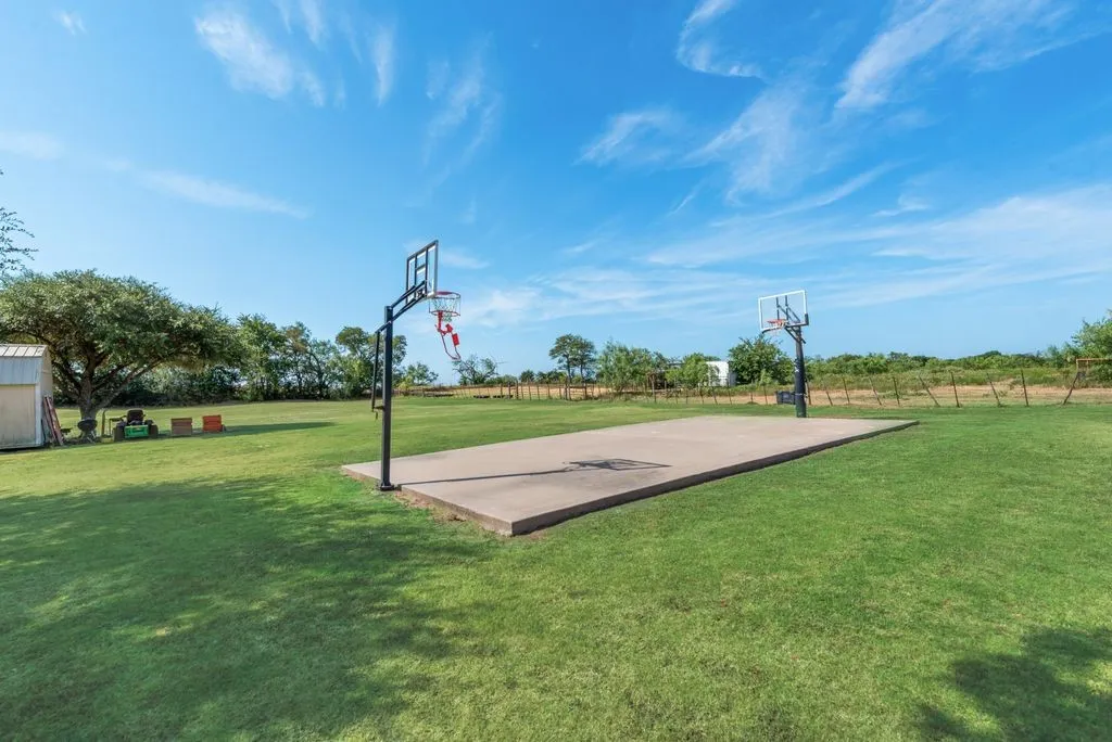 Expansive outdoor space featuring a concrete sports court with two basketball hoops, a detached storage shed, and mature trees