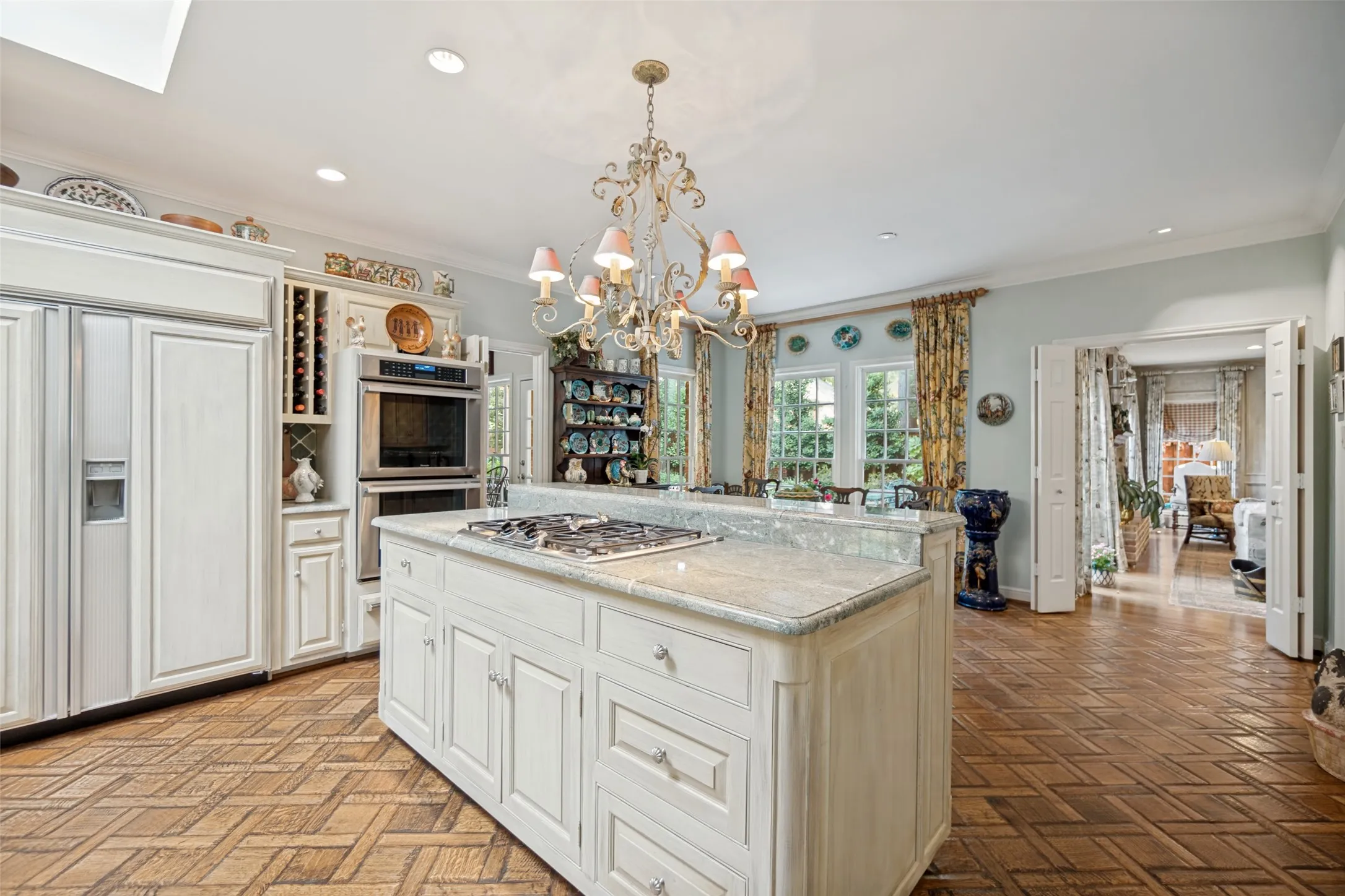 Kitchen featuring a central island with a gas cooktop, built-in double ovens, integrated refrigerator, wood-finish flooring, and decorative chandelier lighting
