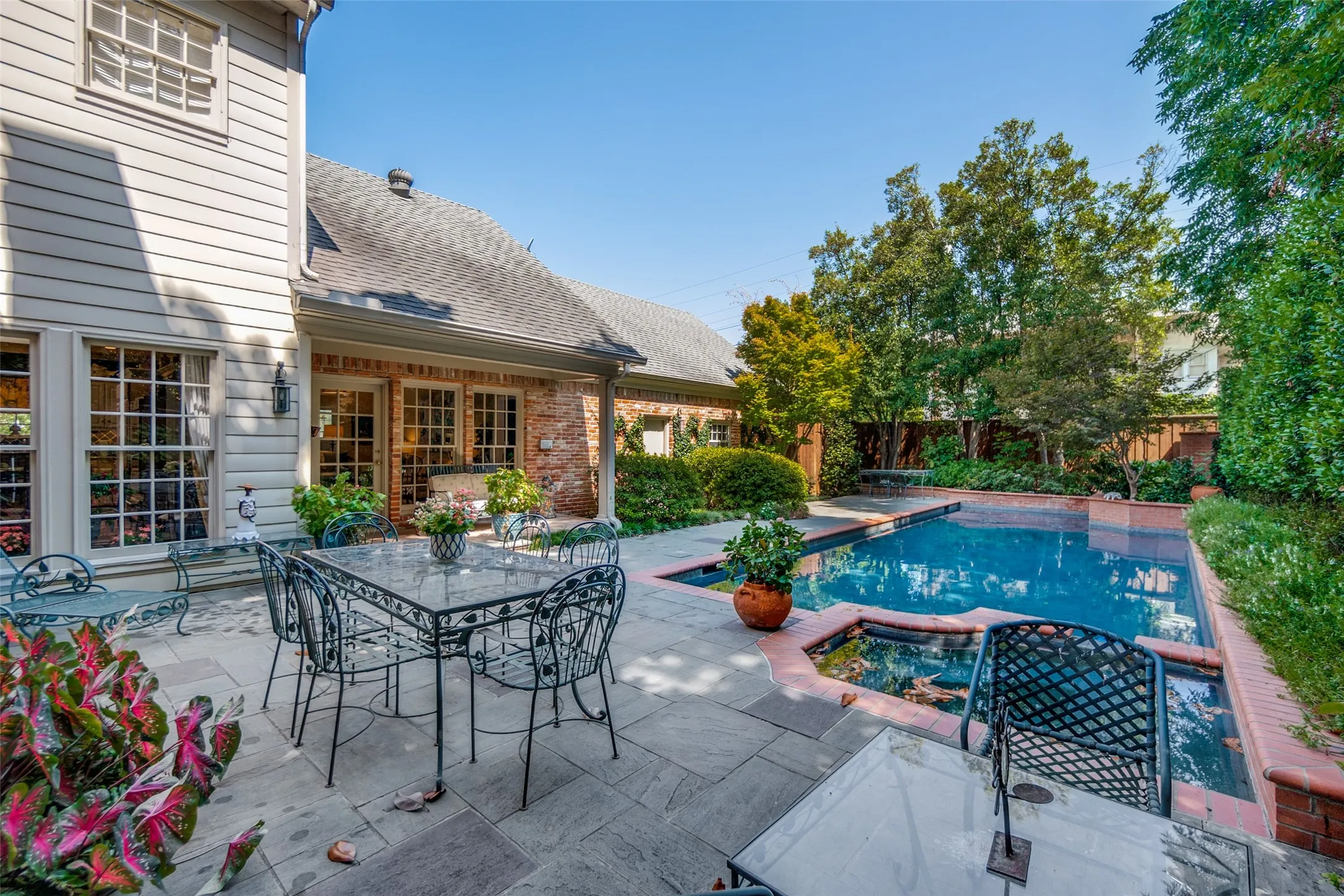 Expansive outdoor patio with a rectangular swimming pool, integrated spa, and mature landscaping