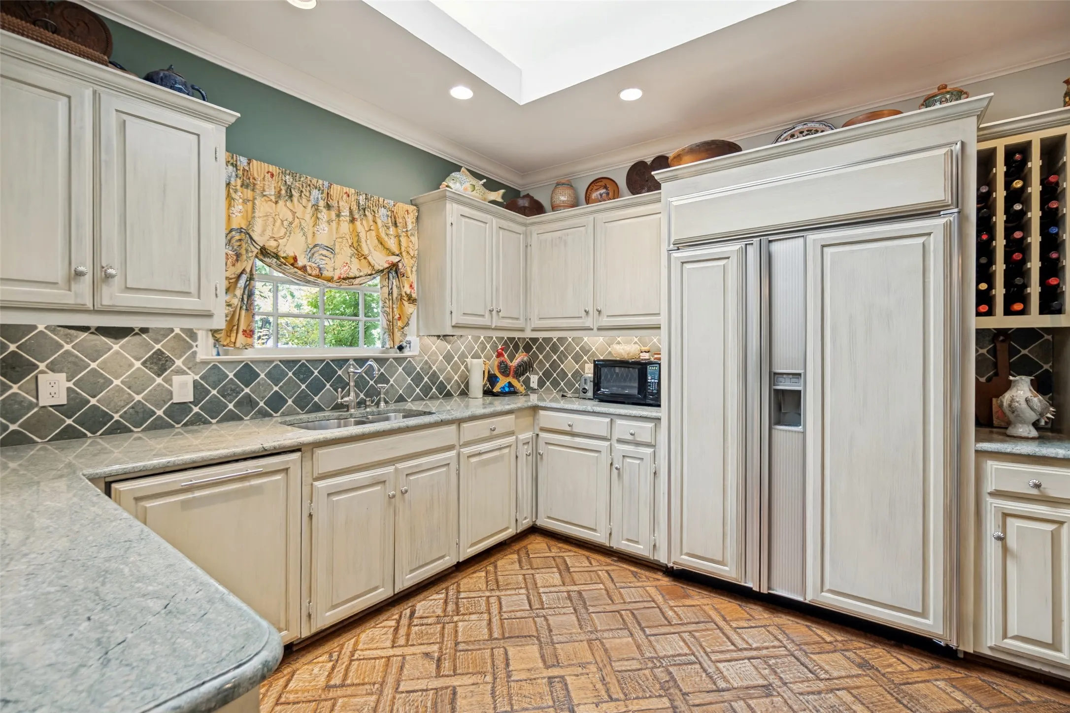 Kitchen featuring wood-finish flooring, light-toned cabinetry, light-toned countertops, a full-size stainless steel refrigerator, and a skylight