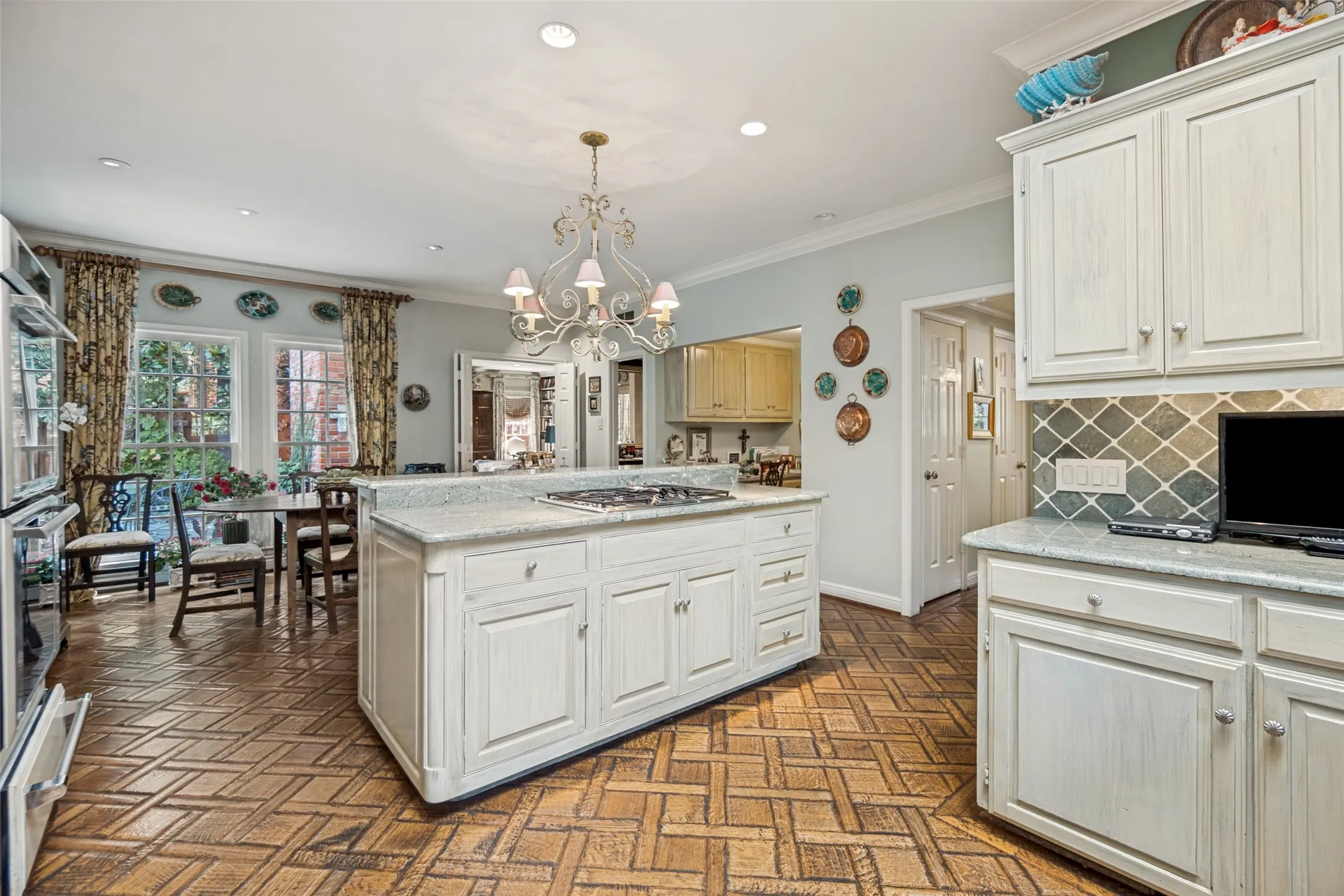 Kitchen featuring a central island with cooktop, white cabinetry, integrated double oven, and patterned wood flooring