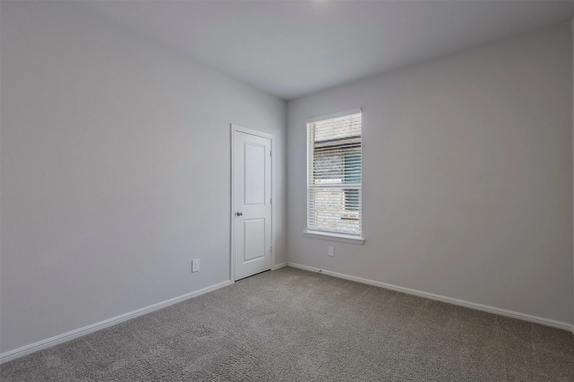 Neutral tone wall finish, textured carpeting, and a window with blinds