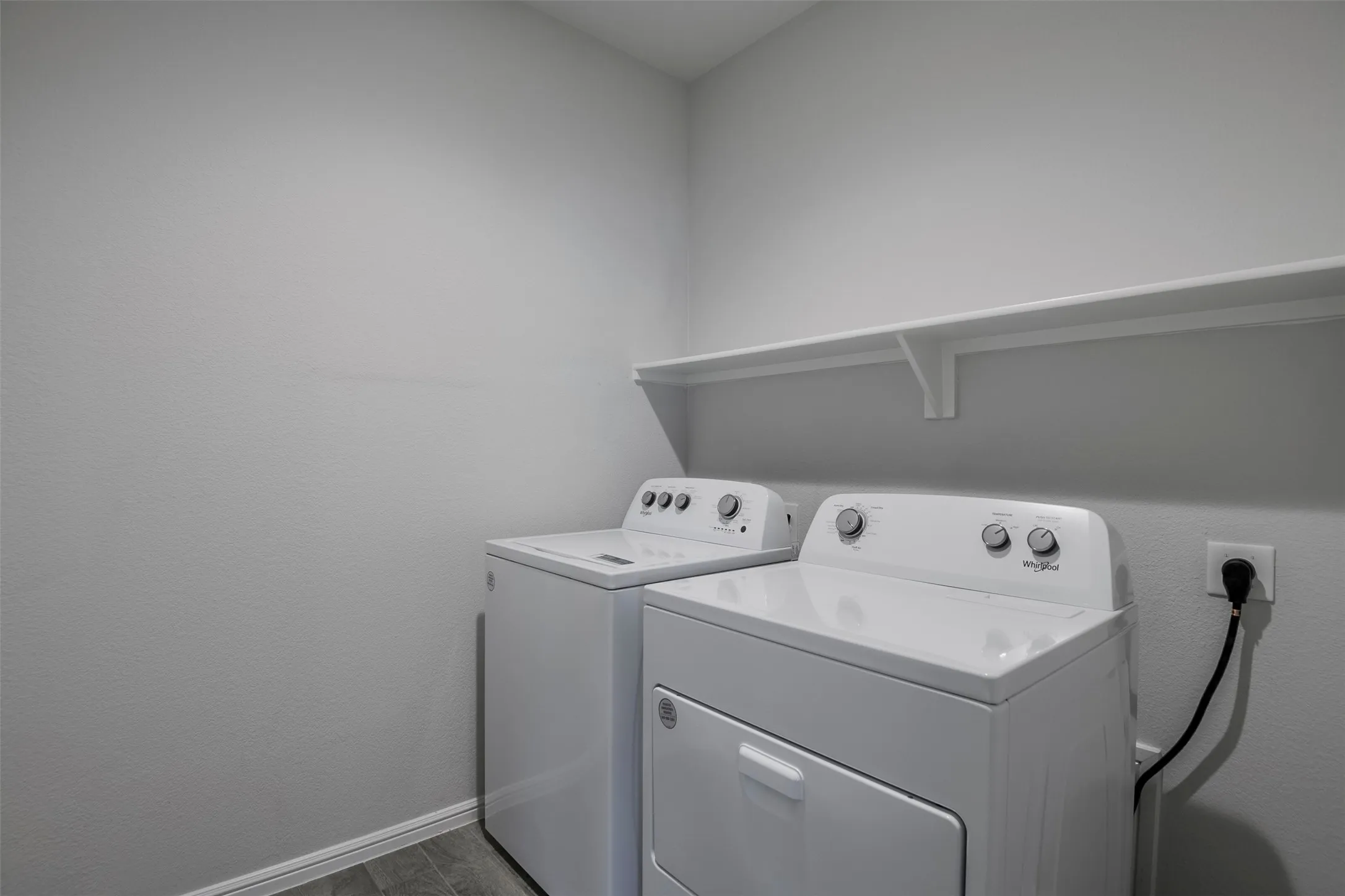 Laundry area featuring a wall-mounted shelf, light-toned walls, and wood-finish flooring