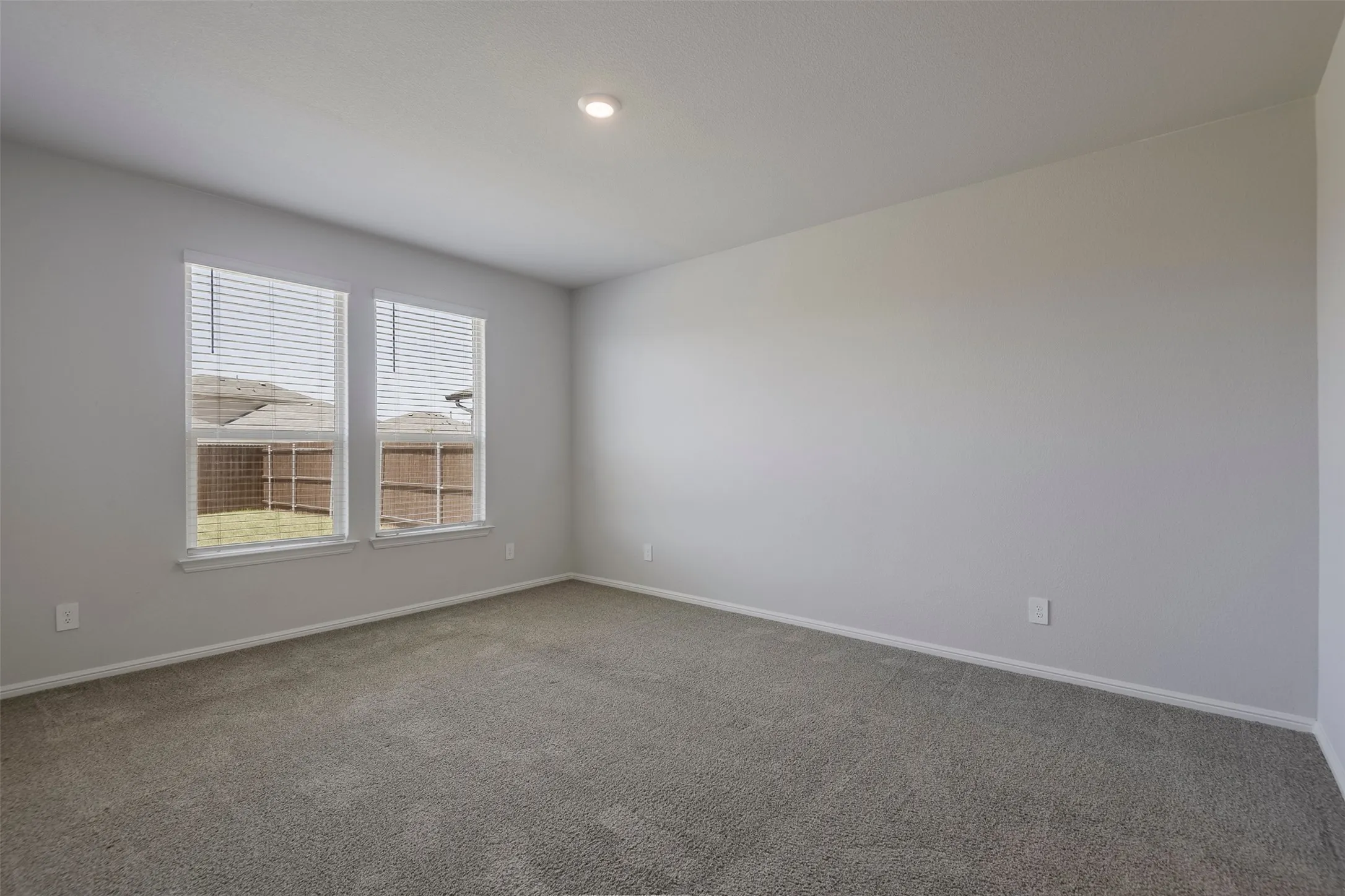 Spacious room featuring neutral carpeting, two windows with blinds, and recessed lighting
