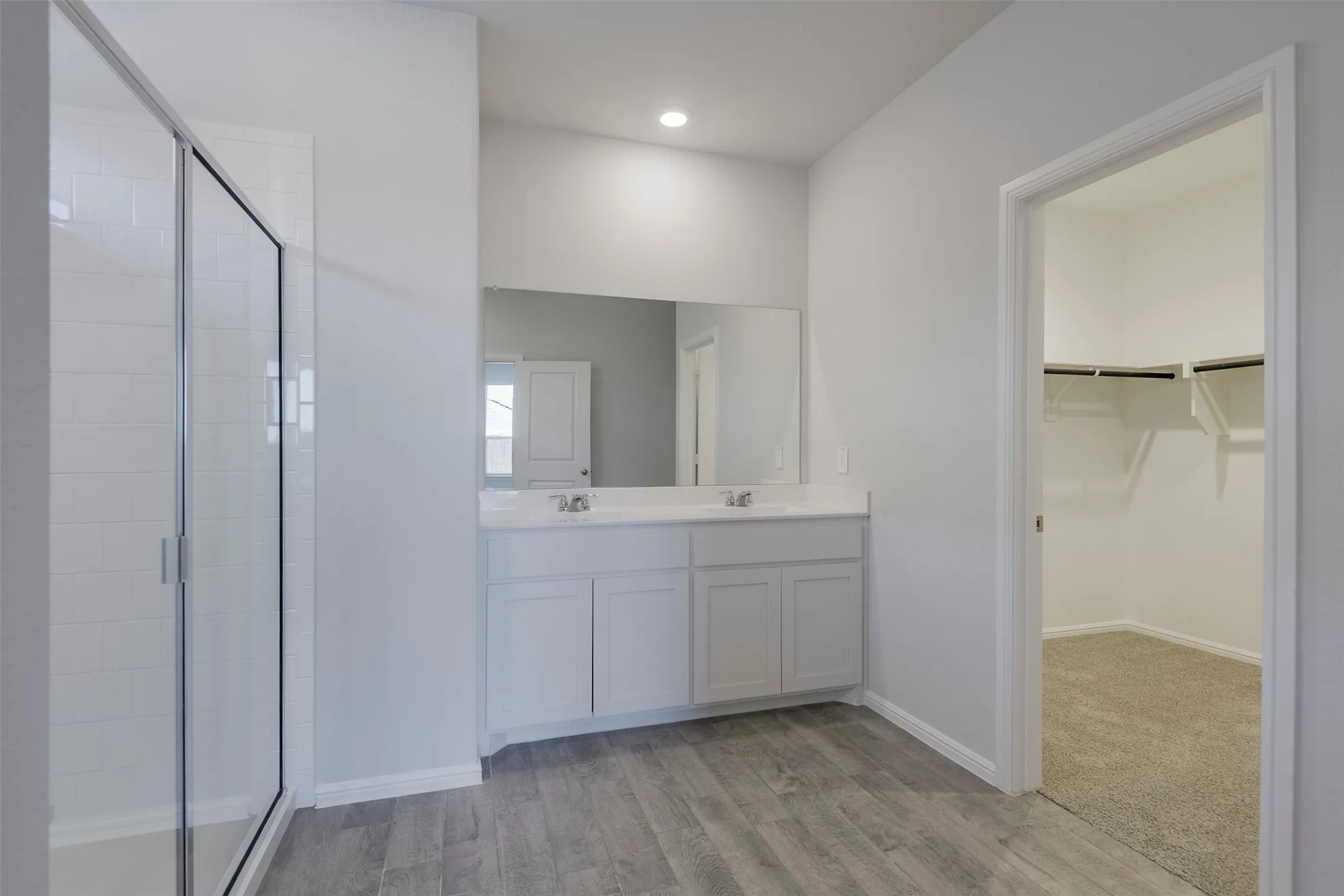 Dual vanity with undermount sinks, wood-finish flooring, glass-enclosed shower with subway tile, walk-in closet with shelving