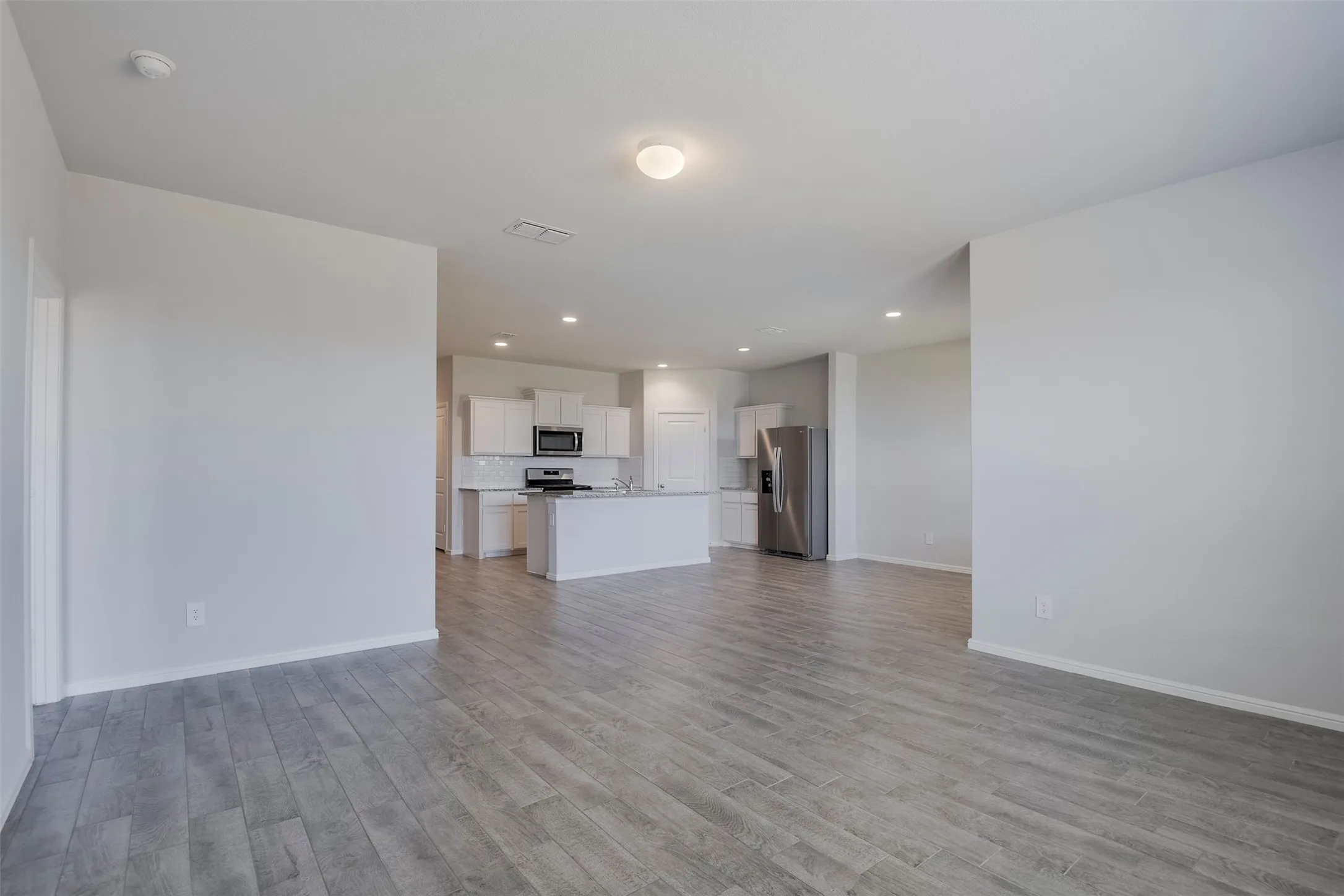 Open-concept living space featuring wood-finish flooring, recessed lighting, and a kitchen with white cabinetry and stainless steel appliances
