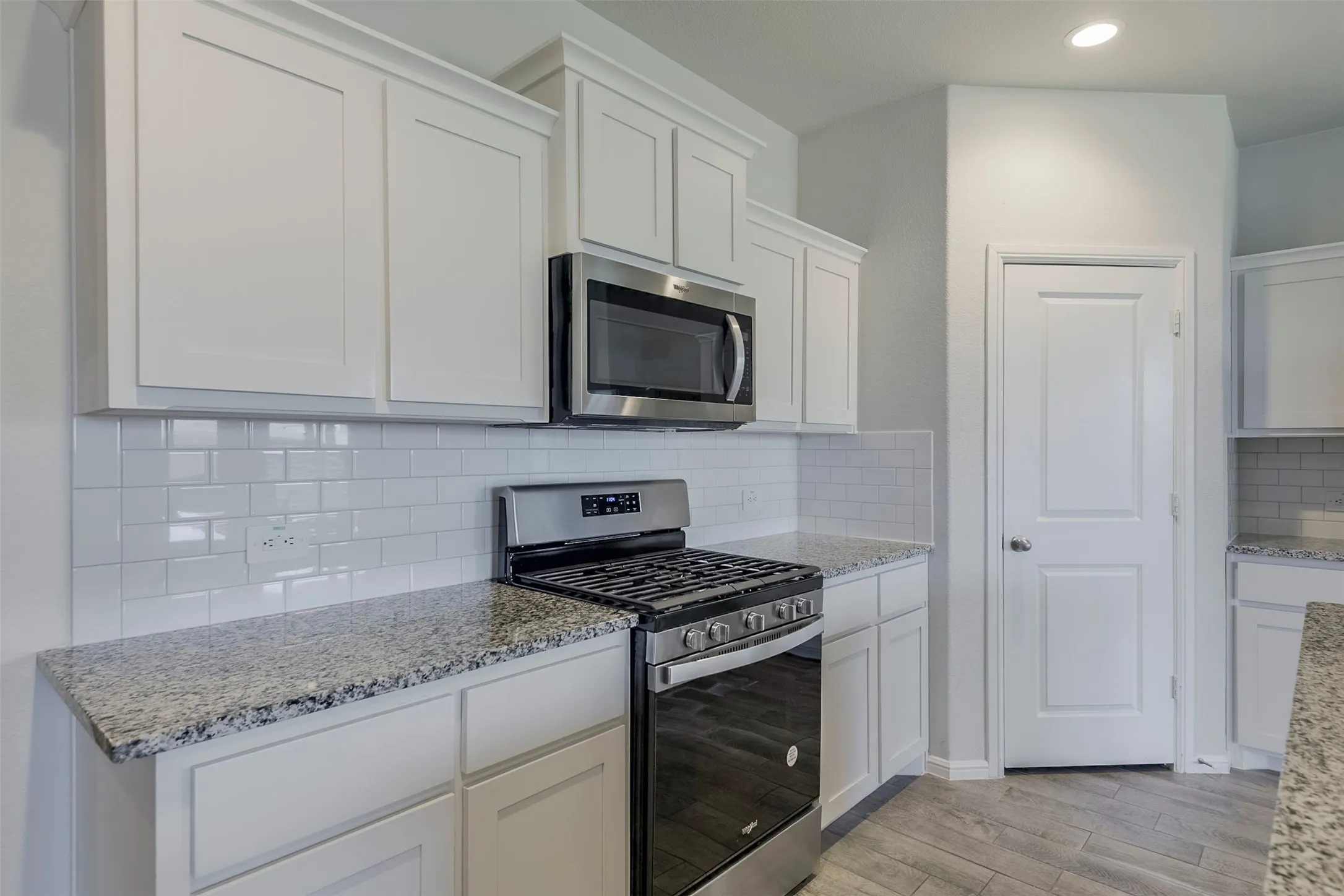 White shaker cabinetry, stainless steel appliances, subway tile backsplash, granite countertops, and wood-finish flooring