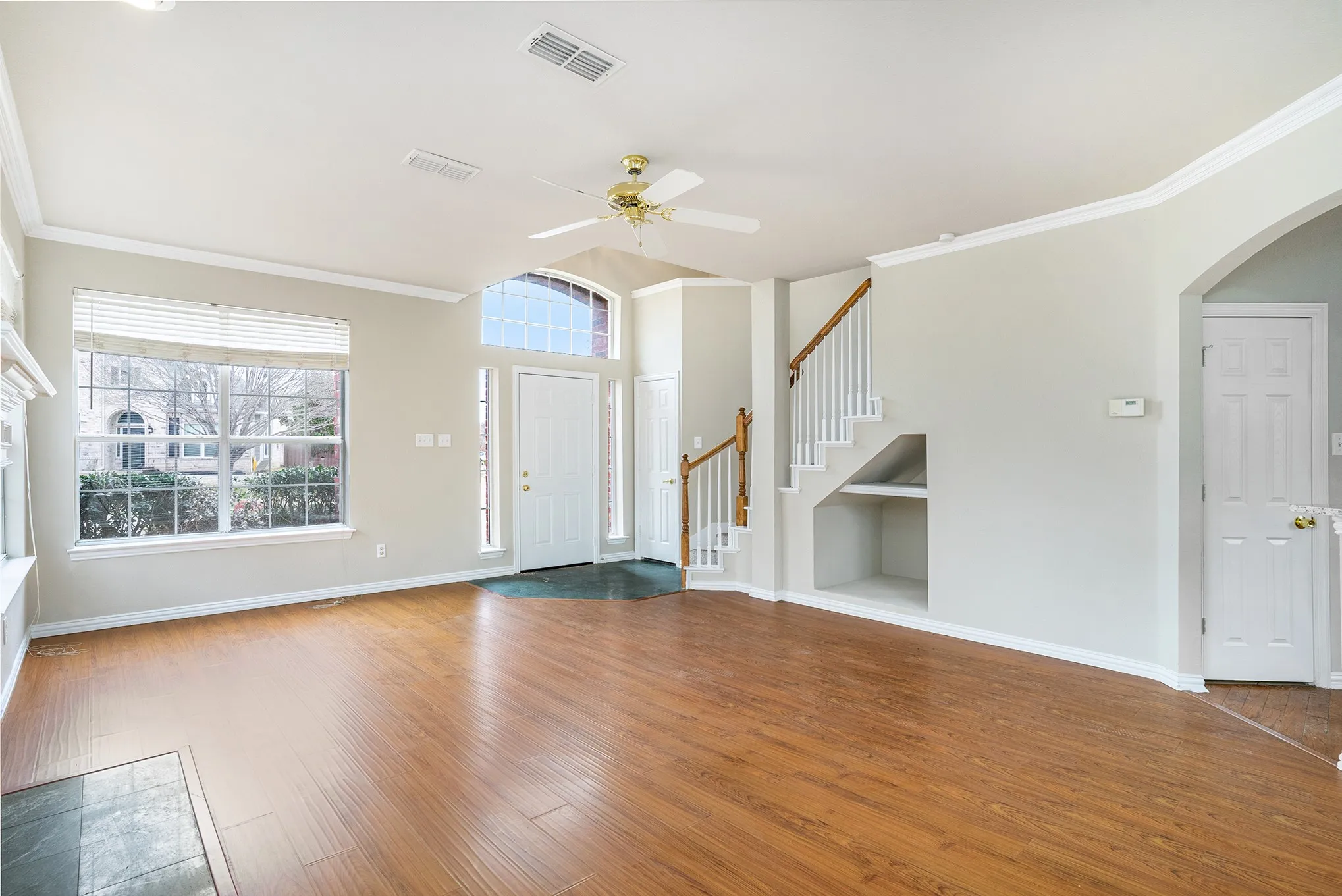 Unfurnished living room featuring crown molding, built in shelves, wood-type flooring, and ceiling fan
