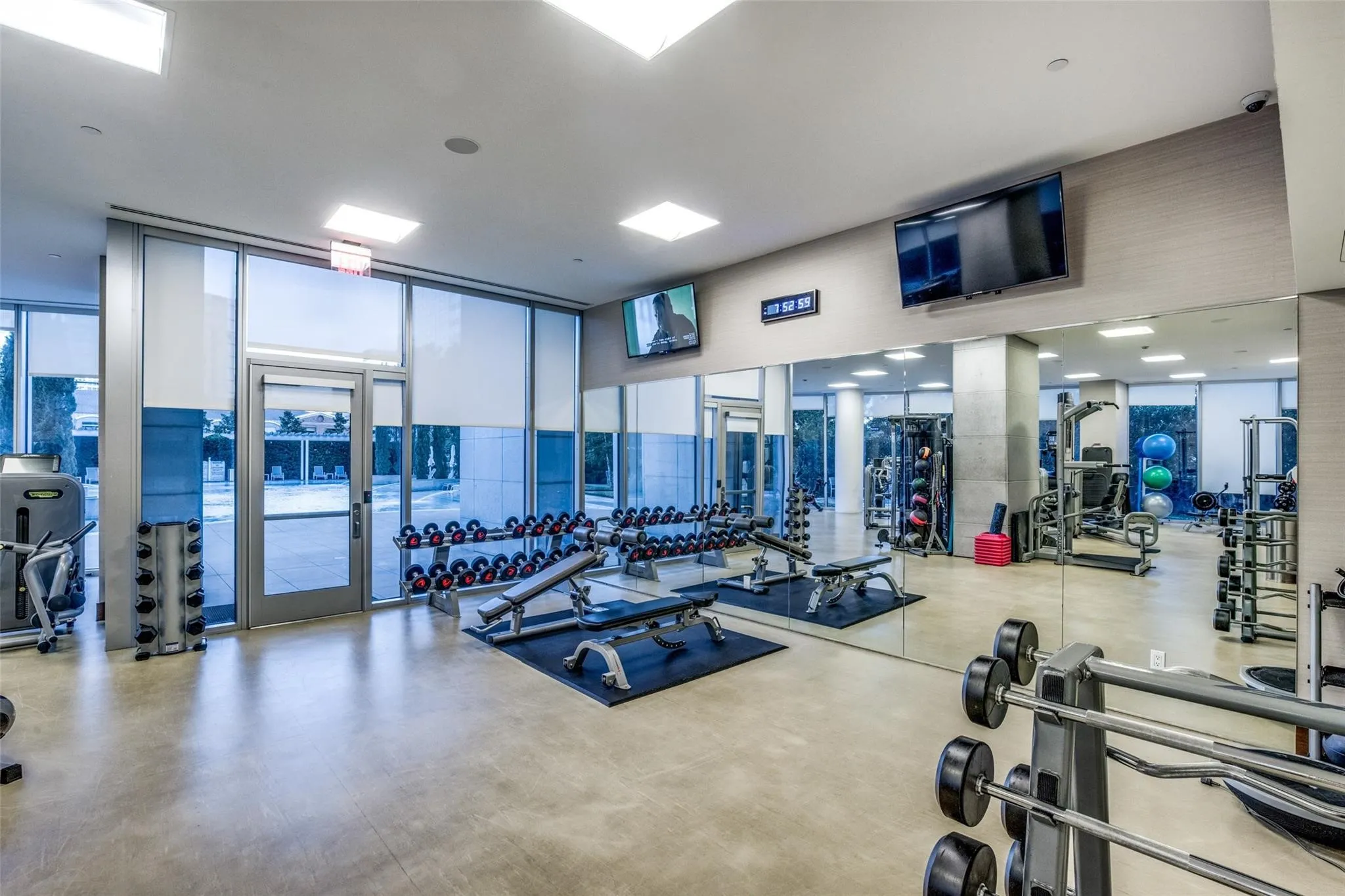 Fitness center with a concrete-finish floor, floor-to-ceiling windows, mirrored wall, recessed lighting, and wall-mounted televisions
