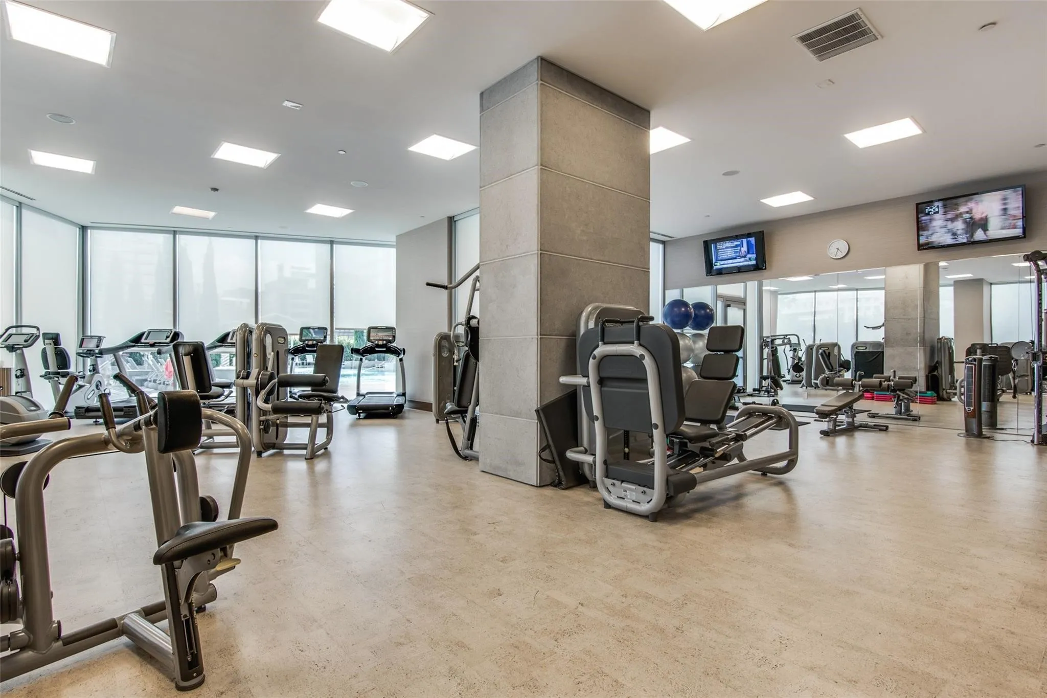 Expansive fitness center featuring commercial-grade equipment, large mirrored wall, multiple wall-mounted screens, and neutral-toned flooring