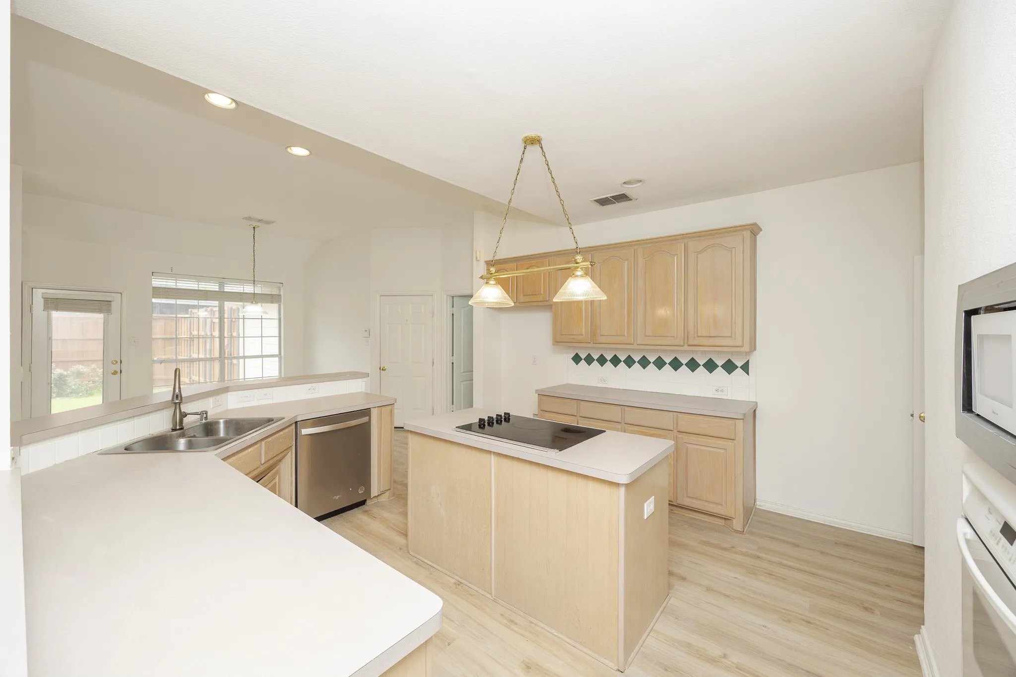 Kitchen with light brown cabinetry, dishwasher, a center island, black electric stovetop, and oven