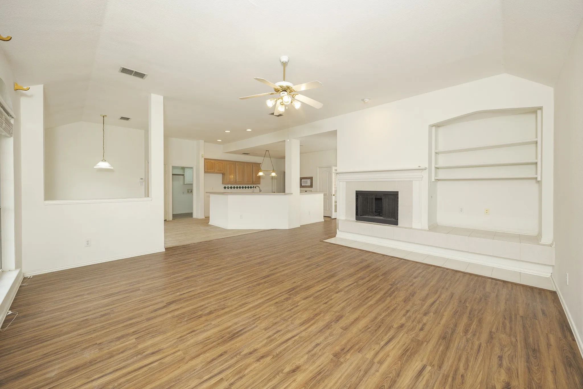 Unfurnished living room with light wood-style flooring, ceiling fan, a fireplace, and vaulted ceiling