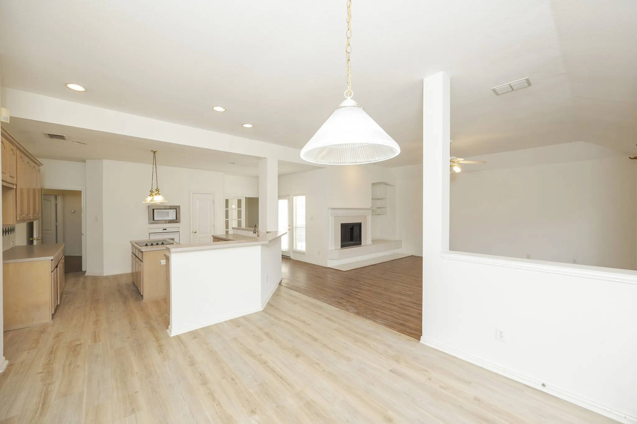 Kitchen featuring white microwave, light wood-style floors, recessed lighting, open floor plan, and a fireplace with raised hearth