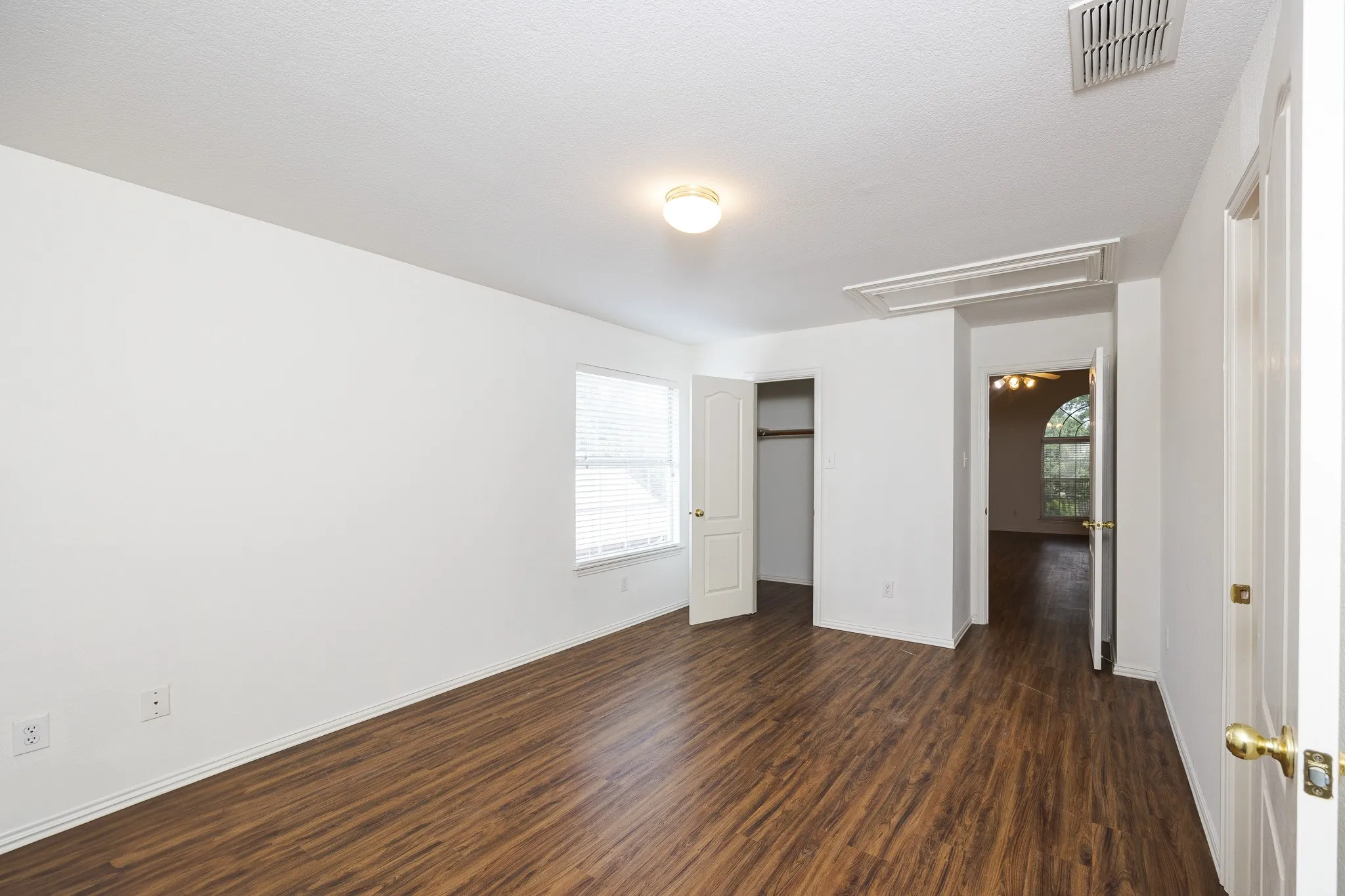 Unfurnished bedroom featuring attic access, dark wood-style flooring, multiple windows, and a closet