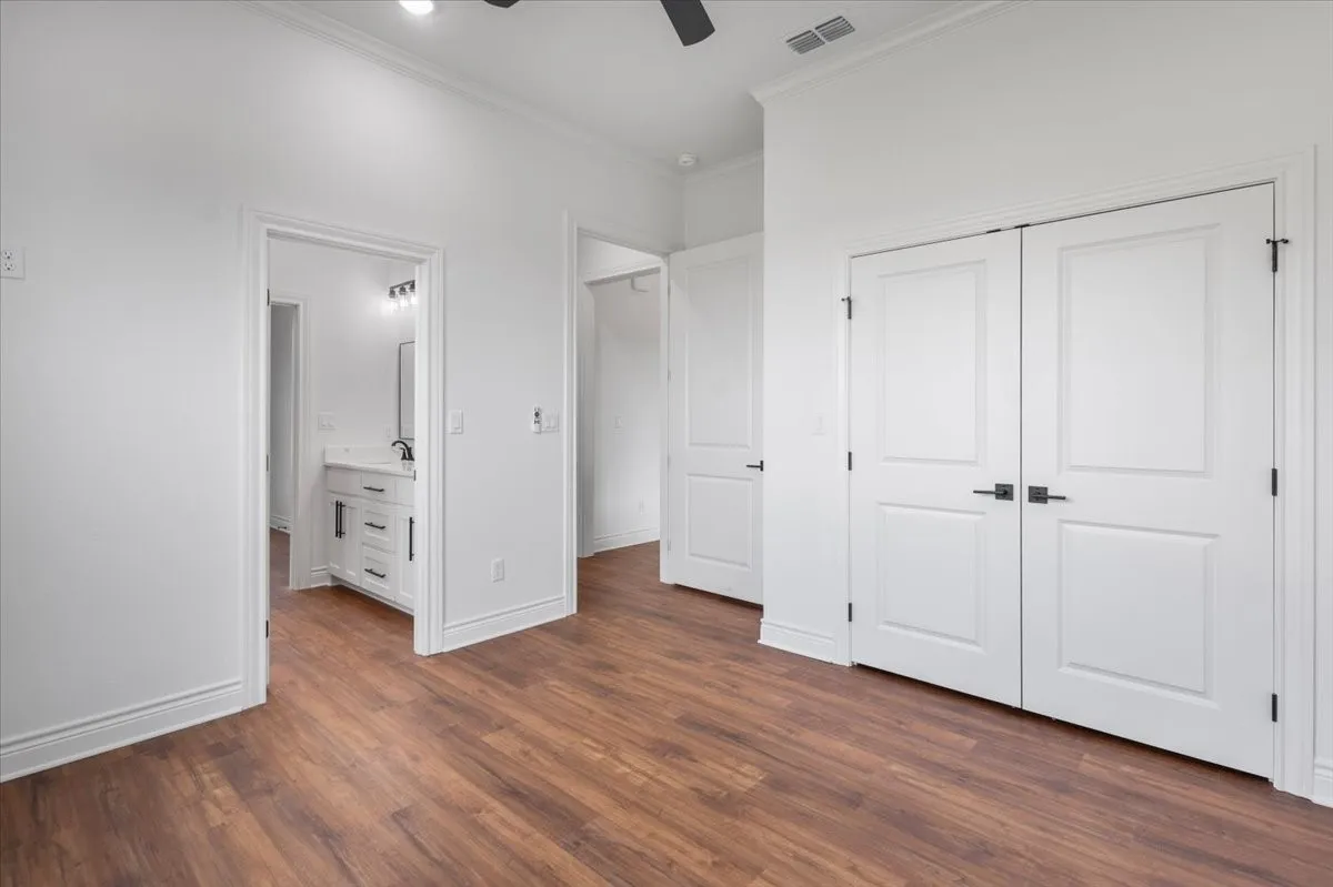 Wood-finish flooring with white trim, double panel doors with matte black hardware, and a ceiling fan