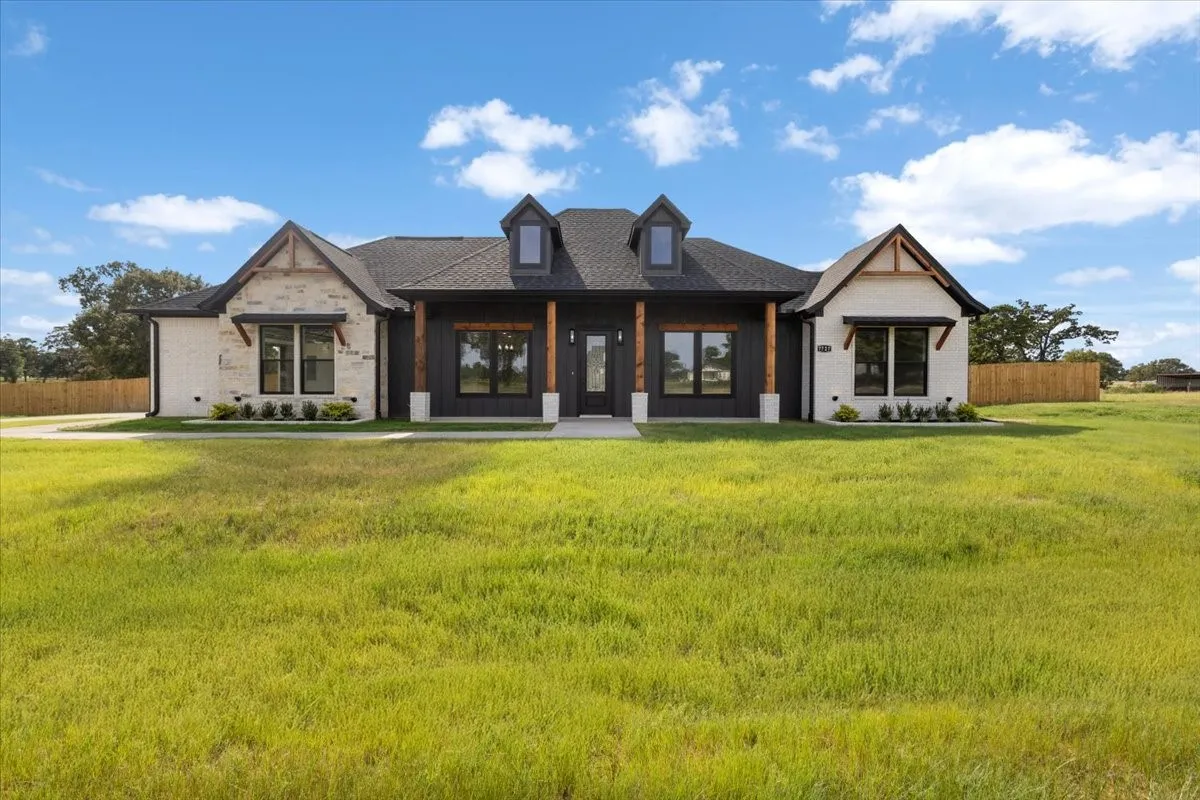 Modern farmhouse residence featuring a striking mixed-material exterior with dark brick and light stone accents, complemented by dual peaked rooflines and decorative dormer windows