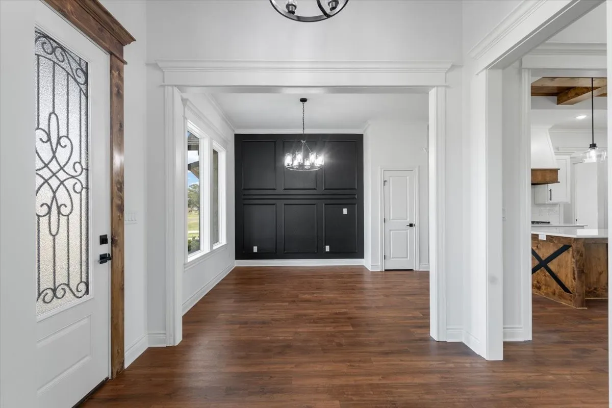 Decorative glass entry door with wood-finish trim, wood-finish flooring, accent wall with panel molding, multiple windows, and a chandelier