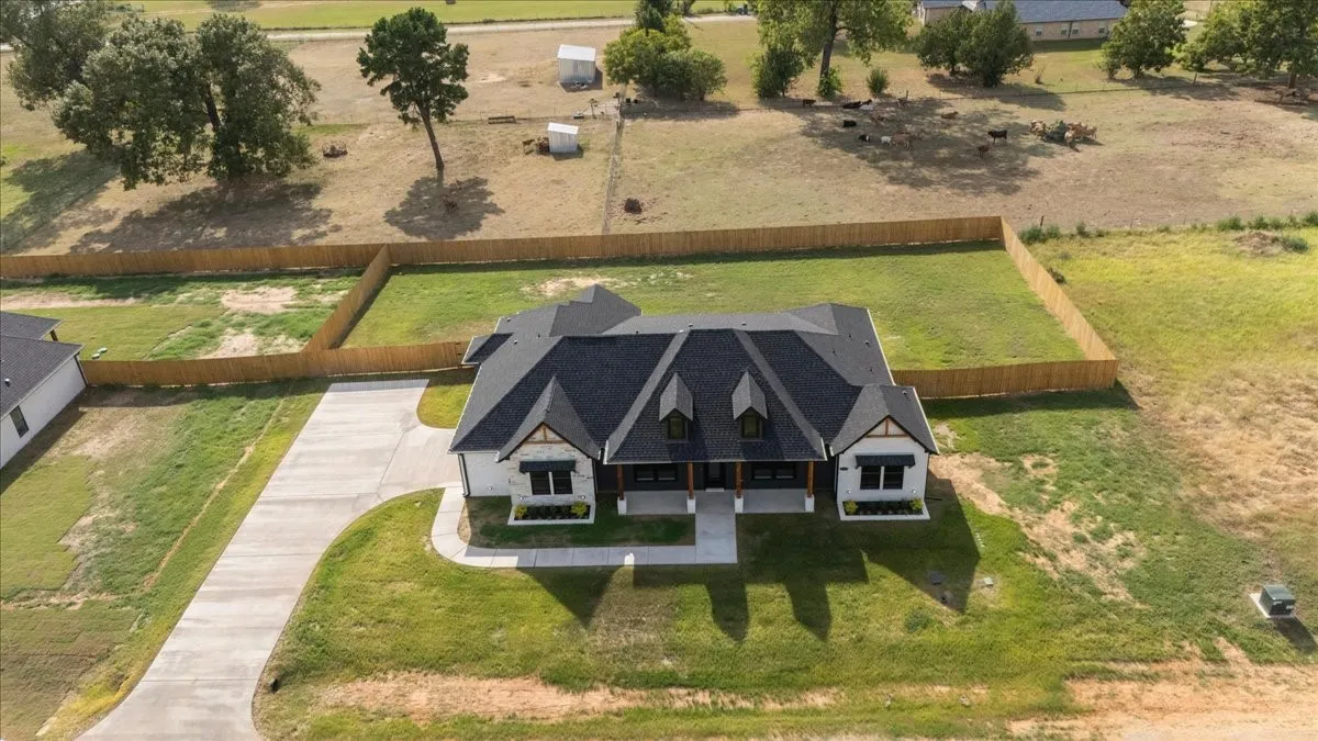 Newly constructed residence featuring a dark shingle roof, white exterior with stone accents, and a fenced backyard