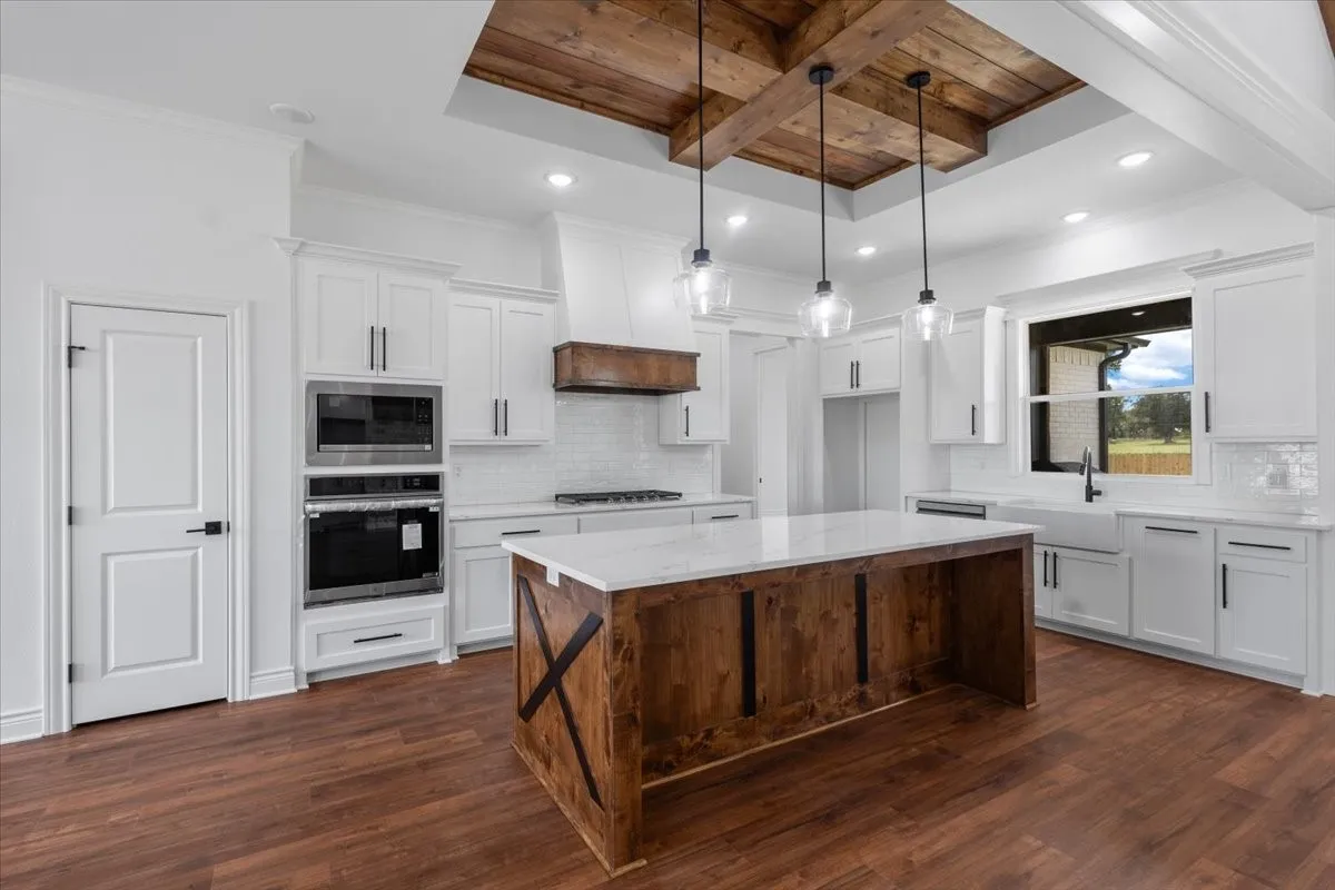 Chef's kitchen featuring white cabinetry with stainless steel appliances, a large wood-finish island with pendant lighting, quartz countertops, and a coffered ceiling with recessed lighting