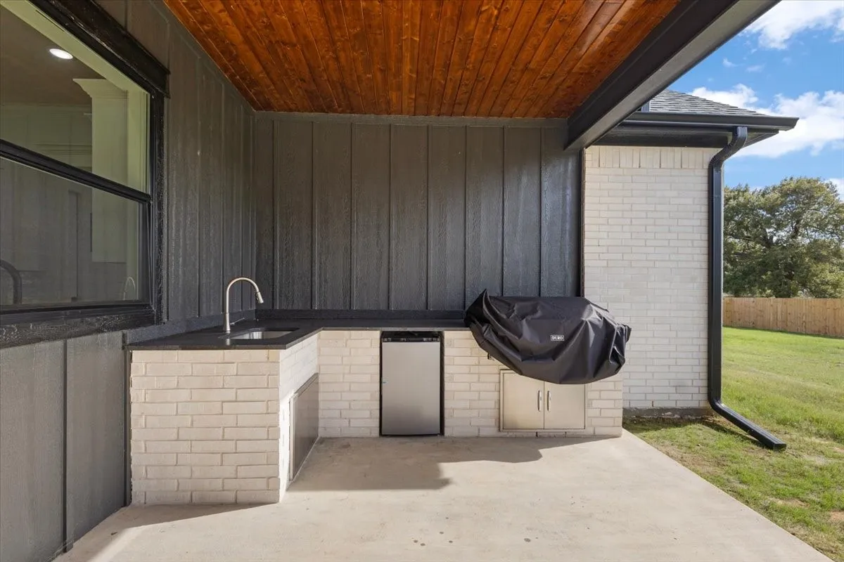 Outdoor kitchen featuring a built-in sink, integrated mini-refrigerator, stainless steel cabinet, light-colored brick base, and dark countertop