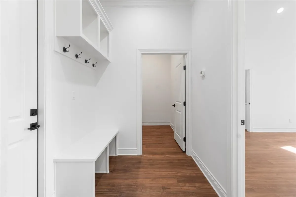 Modern hallway featuring warm wood-finish flooring, clean white walls, and abundant natural light