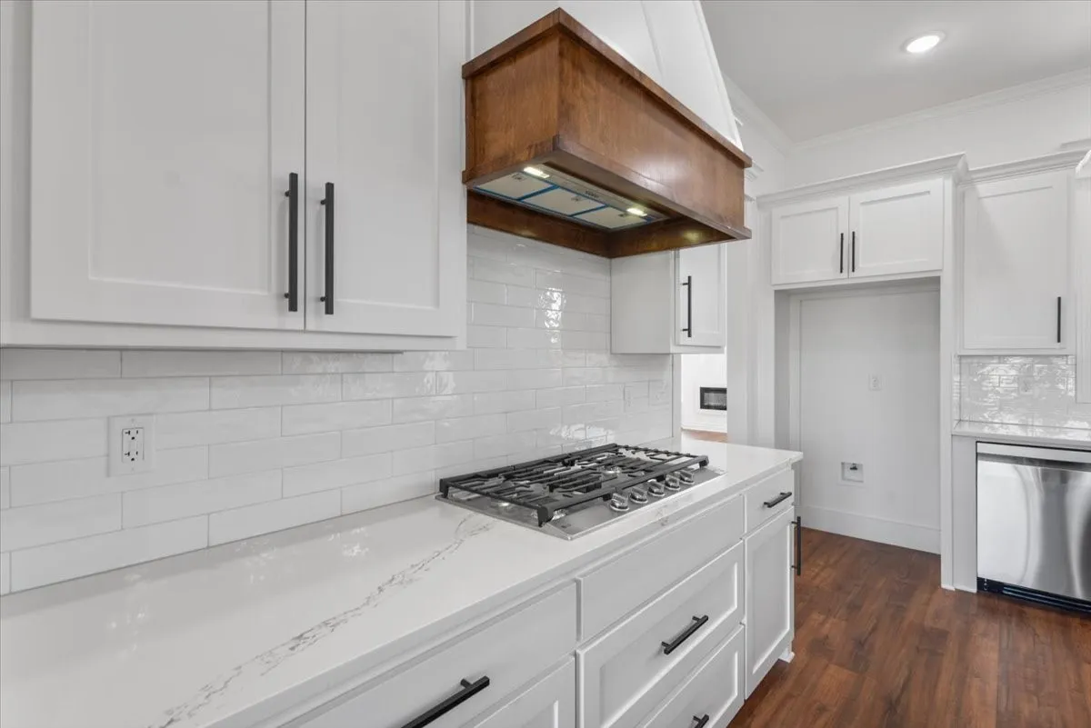 White shaker cabinetry with matte black hardware, quartz countertops, white subway tile backsplash, stainless steel gas cooktop, and wood-finish flooring
