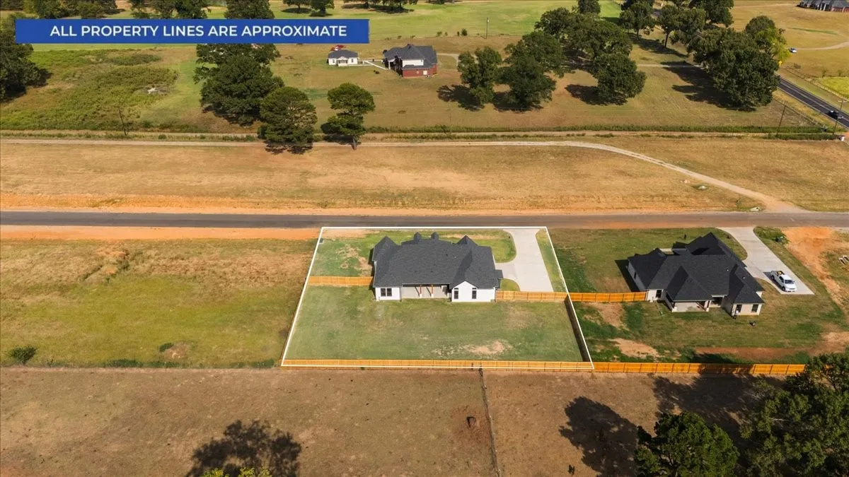 Aerial perspective showcasing a single-family residence with a dark shingle roof, light-toned exterior, and a paved driveway