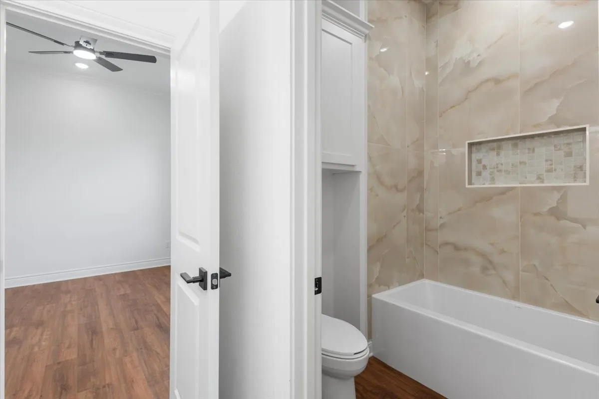 Bathroom featuring a built-in tub, tiled shower surround with a mosaic niche, and wood-finish flooring