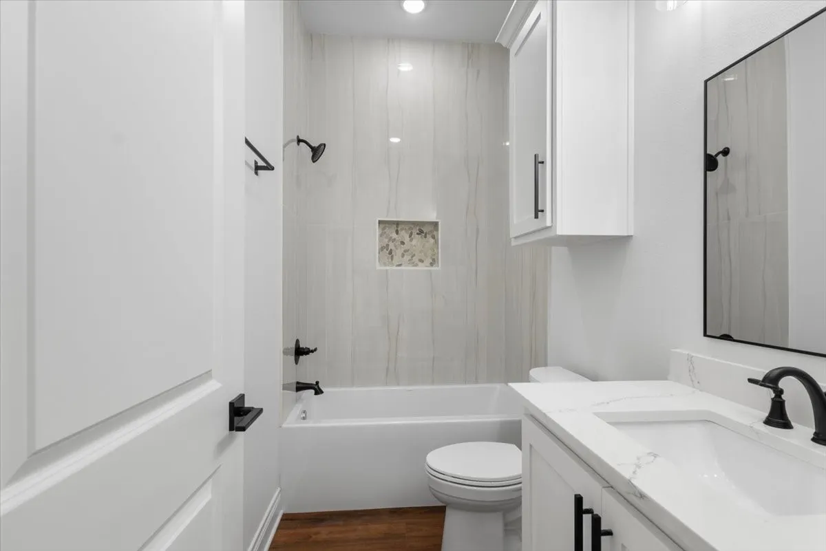 Full bathroom featuring a white vanity with a white countertop and integrated sink, matte black fixtures, a built-in tub with tile surround, and a recessed shower niche