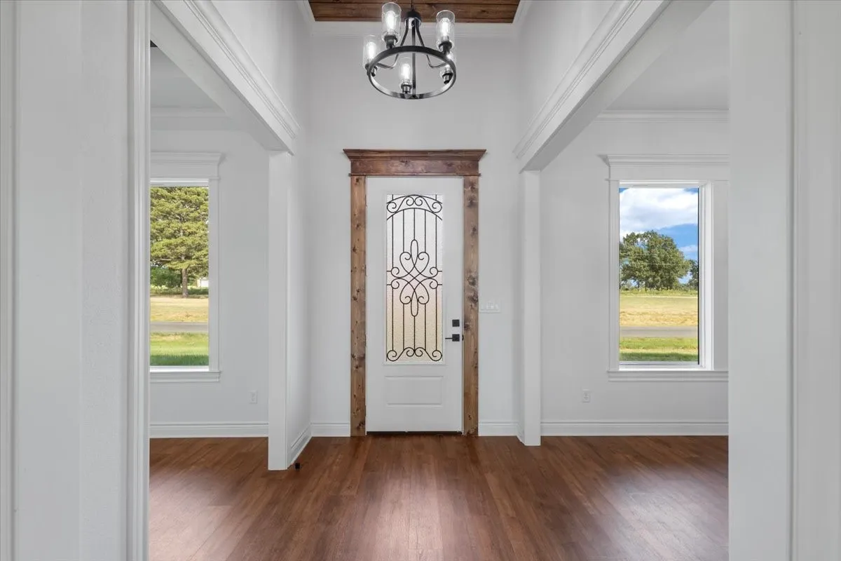 Entryway featuring wood-finish flooring, decorative glass entry door with wood-finish trim, and a chandelier with exposed bulbs
