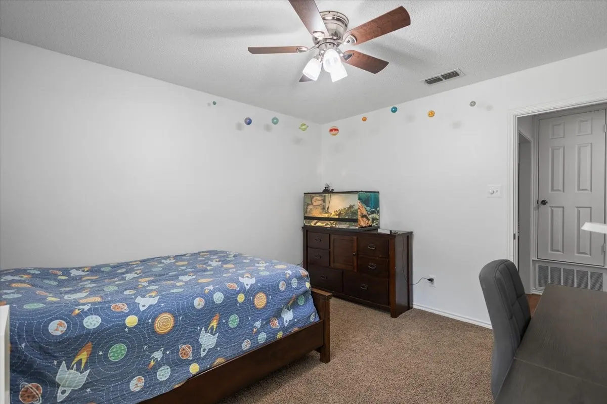Bedroom featuring neutral wall paint, textured carpet flooring, and a ceiling fan with integrated lighting