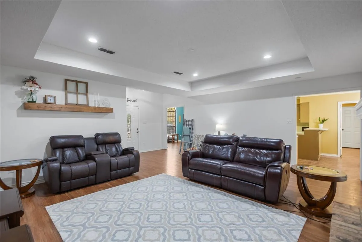 Spacious living area featuring wood-finish flooring and a tray ceiling with recessed lighting