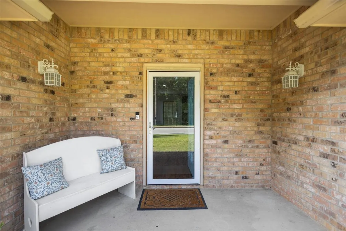 Brick facade entry with a full-light storm door, white sconce lighting, concrete flooring, and a recessed ceiling