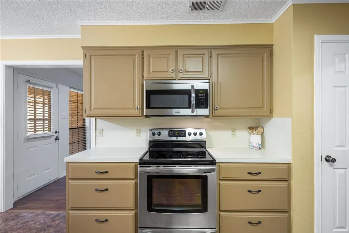 Kitchen featuring a stainless steel electric range, stainless steel microwave, light-colored cabinetry, white countertops, and white backsplash