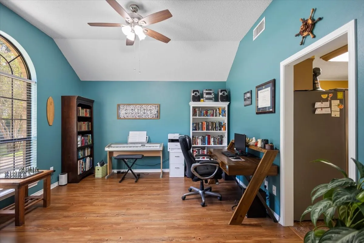 Vaulted ceiling room featuring wood-finish flooring, an arched window, and a ceiling fan