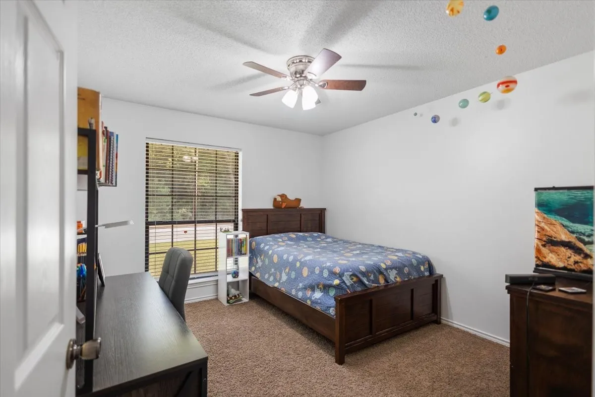 Carpeted interior room featuring a window with horizontal blinds, a ceiling fan with integrated lighting, and white baseboards