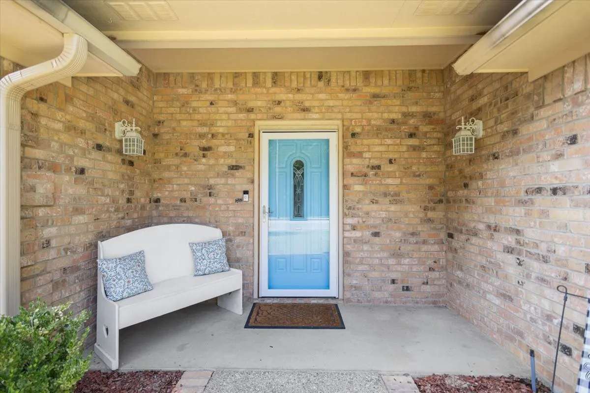 Brick facade entry with a bright blue storm door, twin exterior wall lanterns, and a concrete porch with a finished ceiling
