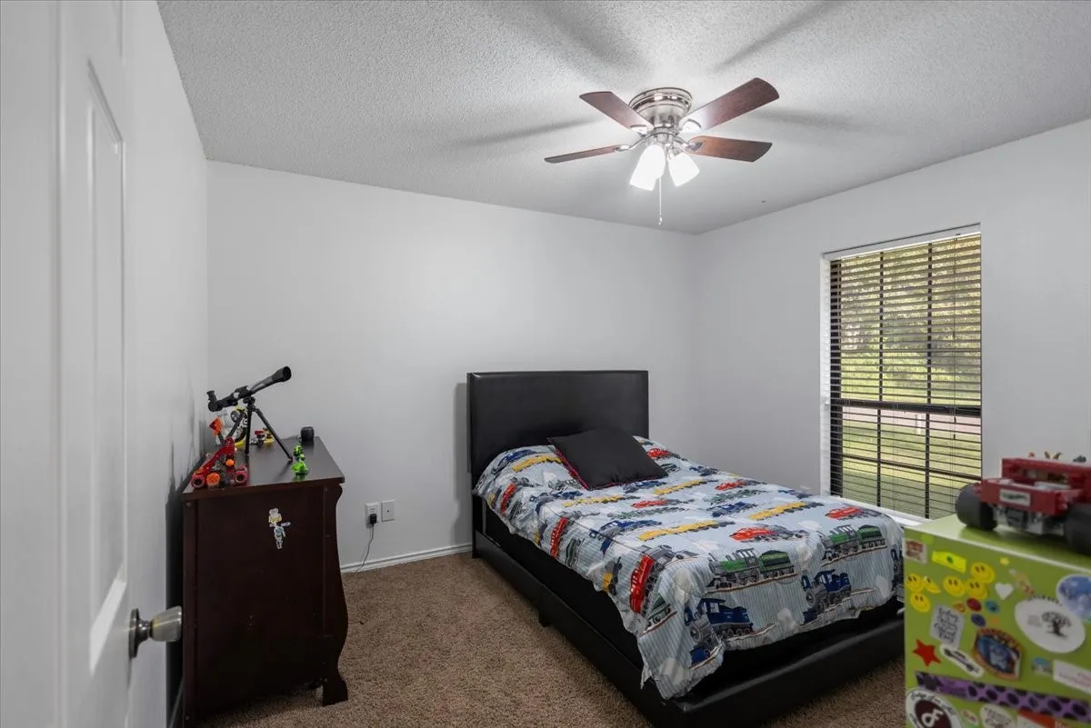 Carpeted bedroom featuring a ceiling fan with light fixture, window with horizontal blinds, and neutral wall paint
