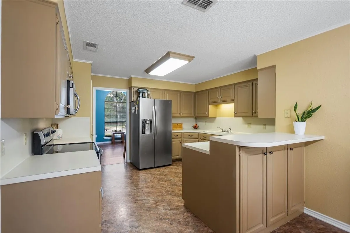 Kitchen featuring tan cabinetry, white countertops, stainless steel appliances, and resilient flooring