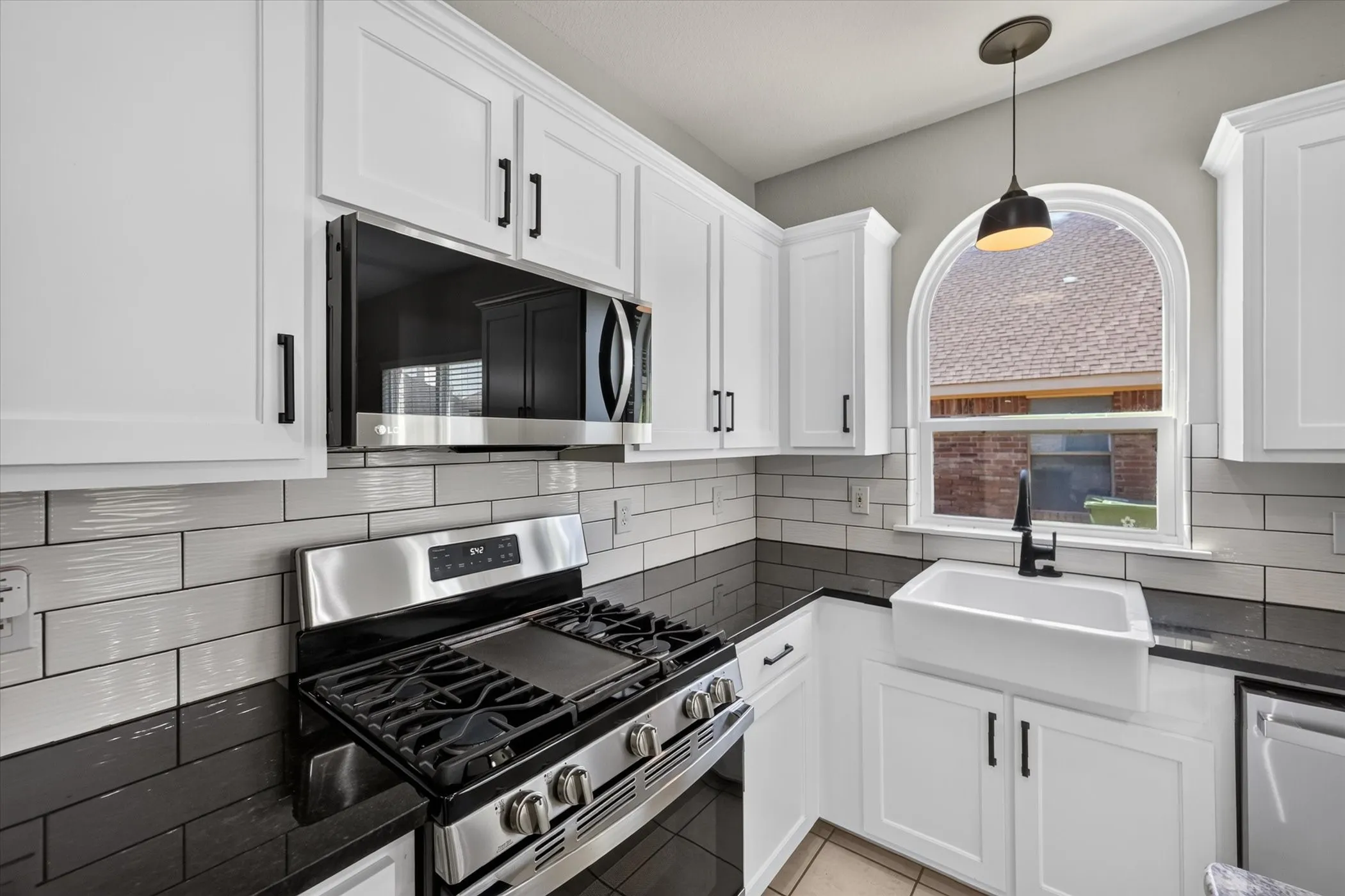 White shaker-style cabinetry with black hardware, stainless steel appliances, black countertops, and a white farmhouse sink