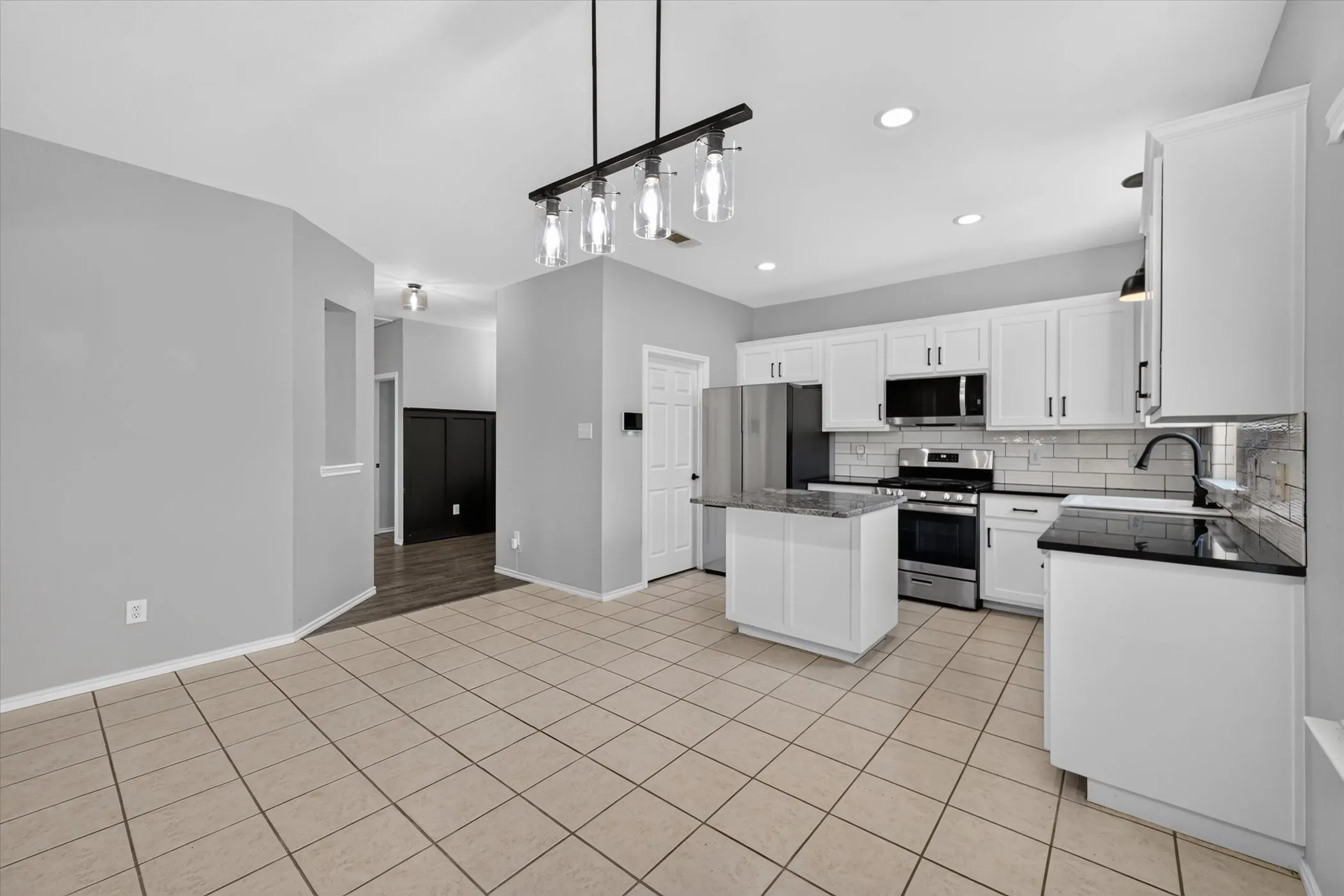 Spacious kitchen with a central island, white cabinetry, dark countertops, and stainless steel appliances